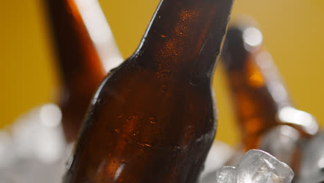 Nahaufnahme-Von-Glasflaschen-Mit-Kaltem-Bier-Oder-Alkoholfreien-Getränken,-Die-In-Einem-Mit-Eis-Gefüllten-Eimer-Vor-Gelbem-Hintergrund-Kühlen-2